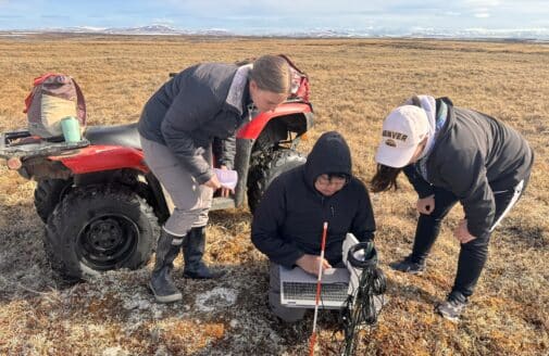 Tiffany Windholz, Reggie Tuluk, Permafrost Pathways Tribal Liaison for the Native Village of Cev’aq, and Darcy Peter downloading data from a temperature sensor.